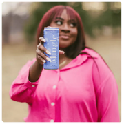 Woman in pink shirt holding a can of Mingle blackberry bellini mocktail outdoors.