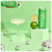 margarita mocktail with lime being poured into a cocktail glass, with a can, lime, and decorative disco balls on a green background