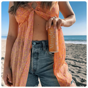 orange mimosa mocktail being held by a woman on a sunny beach.