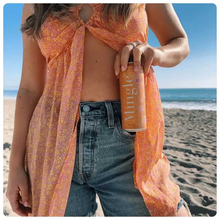 orange mimosa mocktail being held by a woman on a sunny beach.