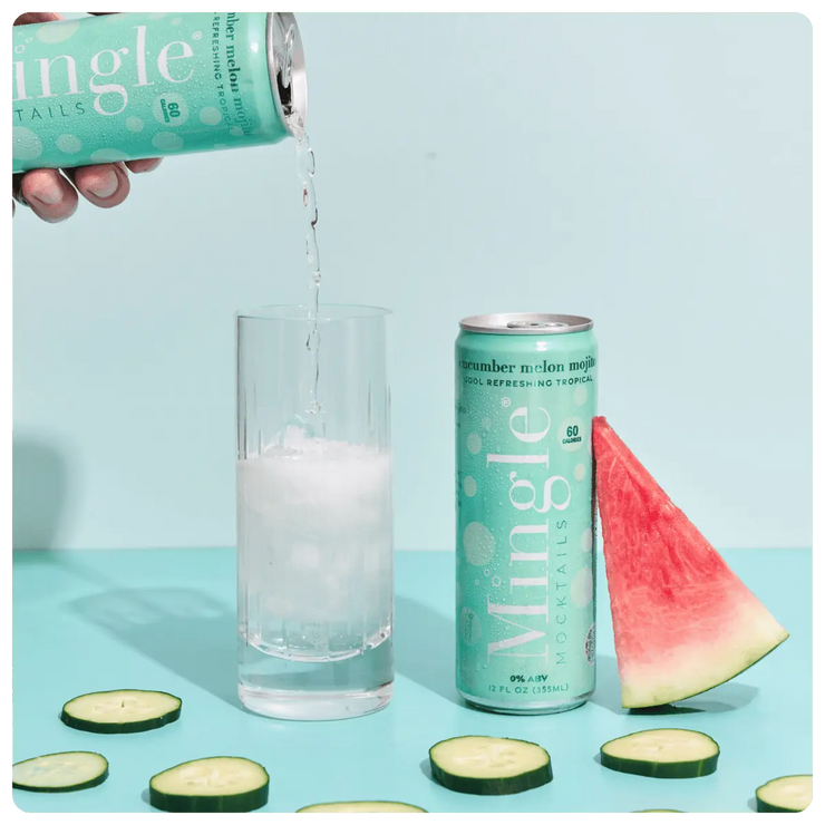 non alcoholic cucumber mojito cocktail being poured into a glass, with cucumber slices, and a watermelon slice on a blue background