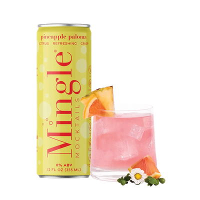 Mingle Mocktails Pineapple Paloma can alongside a pink cocktail in a glass with ice, garnished with a pineapple wedge, grapefruit slice, and small white flowers. The can is yellow with red text highlighting "citrus, refreshing, crisp" and "0% ABV" on the label. The scene is styled with a bright, fresh, and vibrant aesthetic.