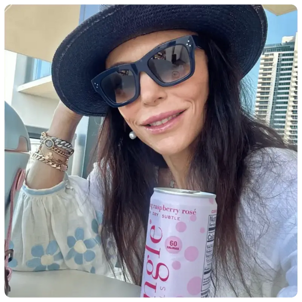 Woman wearing sunglasses & a hat smiling while holding a can of Mingle Mocktails raspberry rosé flavor