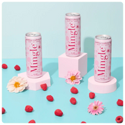 raspberry rosé mocktails being poured into a glass, with cans, fresh raspberries, and flowers arranged on a blue surface