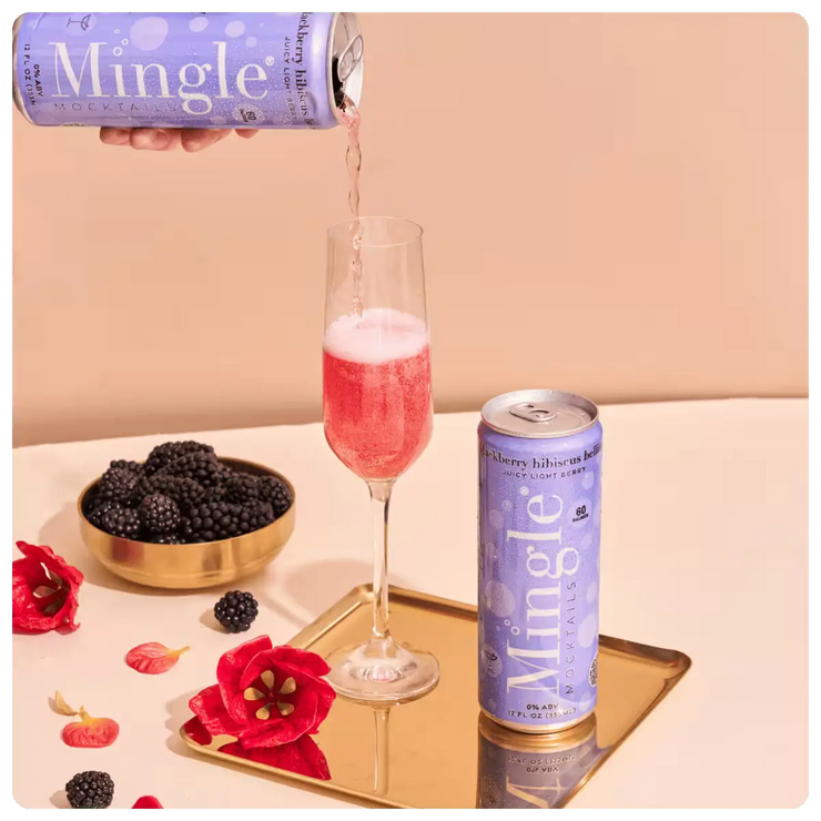 Mingle non-alcoholic blackberry bellini in a champagne flute, accompanied by fresh blackberries and hibiscus flowers.